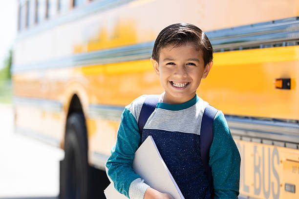 istock Young student with backpack and books stands smiling happily next to a school bus 2242651928