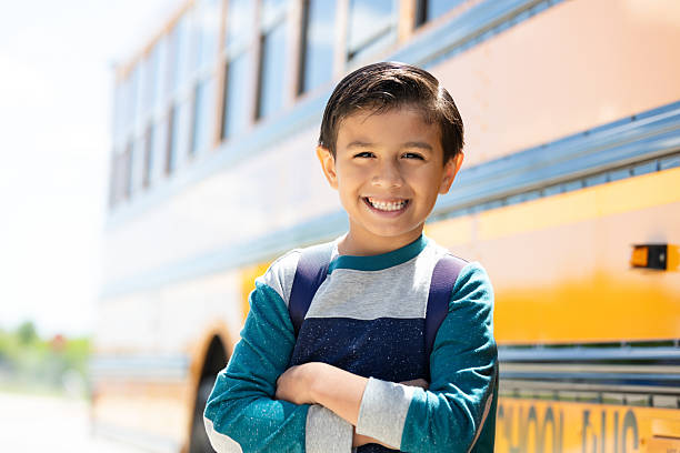 istock Happy young boy with backpack smiling in front of school bus, excited for school. 2242651937