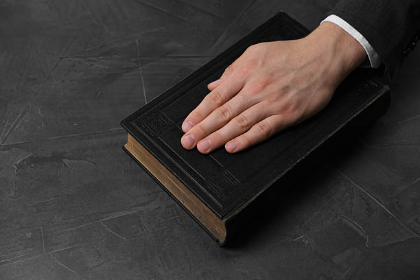 istock Man taking oath with his hand on Bible at black table, closeup 2242658986