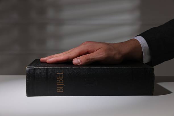 istock Man taking oath with his hand on Bible at white table, closeup 2242658989