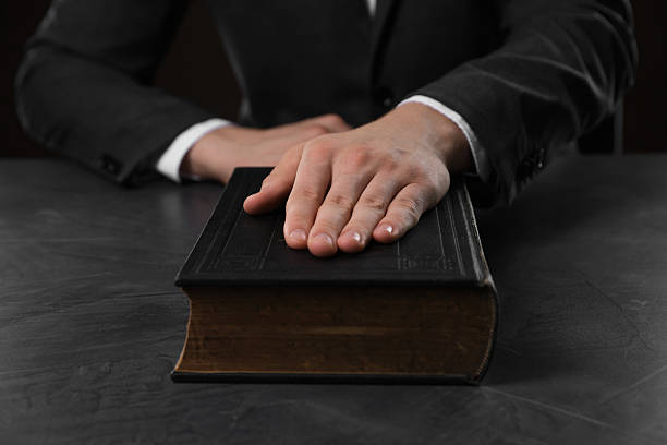 istock Man taking oath with his hand on Bible at black table, closeup 2242658995
