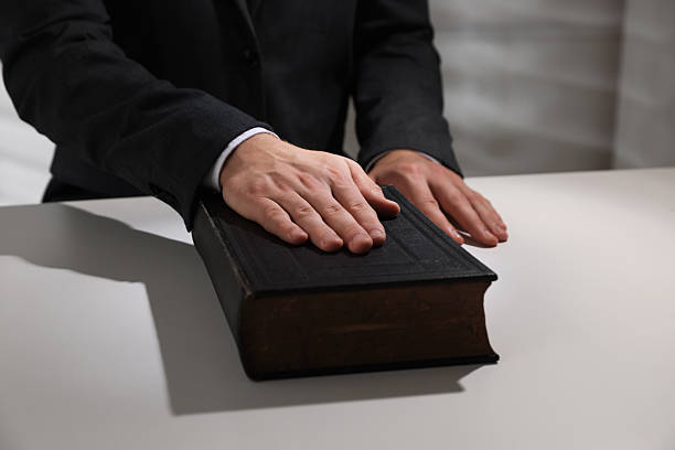 istock Man taking oath with his hand on Bible at white table, closeup 2242659001