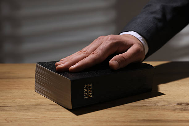 istock Man taking oath with his hand on Bible at wooden table, closeup 2242659004