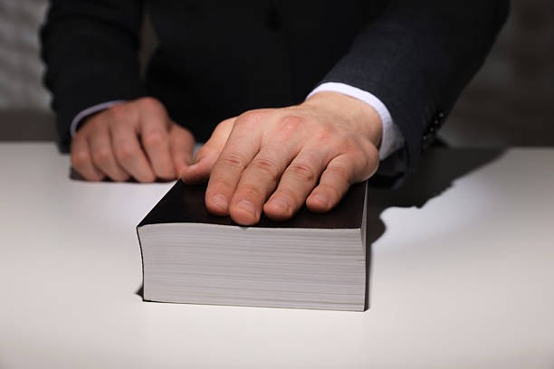 istock Man taking oath with his hand on Bible at white table, closeup 2242659010