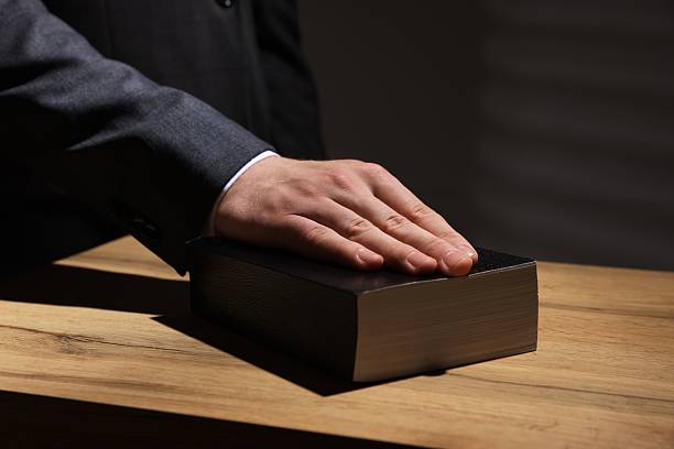 istock Man taking oath with his hand on Bible at wooden table, closeup 2242659012
