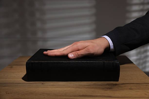 istock Man taking oath with his hand on Bible at wooden table, closeup 2242659015