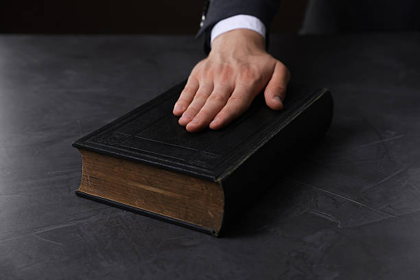 istock Man taking oath with his hand on Bible at black table, closeup 2242659024