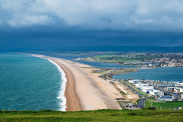 A scenic view of Chesil Beach in Dorset, England, under a dramatic sky.