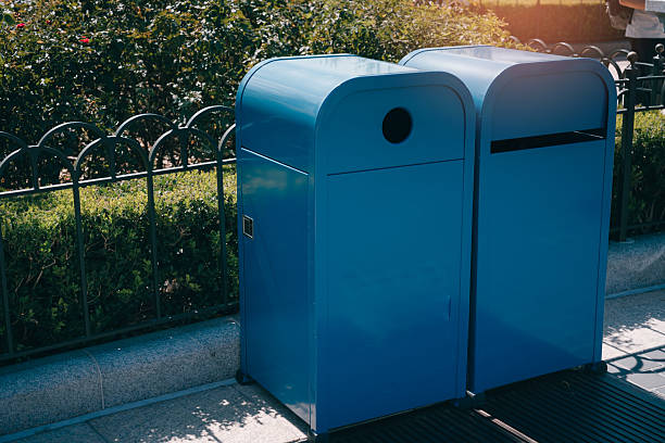 istock Bright Blue Trash Cans in Urban Park Setting Surrounded by Lush Greenery on a Sunny Day 2242659642