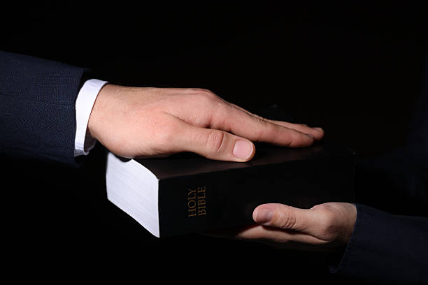 Man taking oath with his hand on Bible against black background, closeup