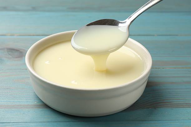 istock Condensed milk flowing down from spoon into bowl on light blue wooden table, closeup 2242662855