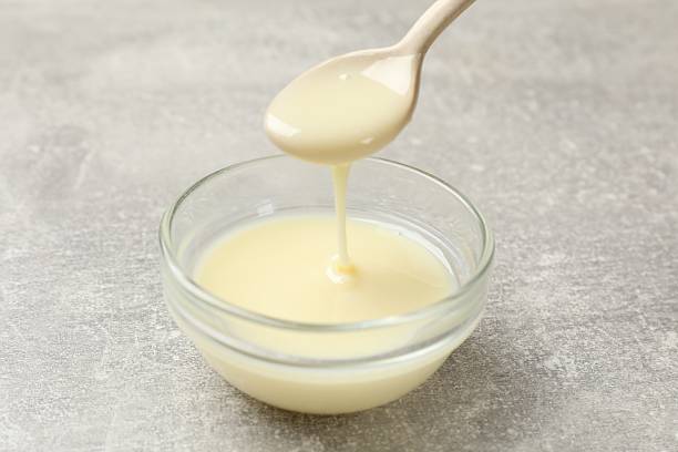 istock Condensed milk flowing down from spoon into bowl on gray textured table, closeup 2242662856