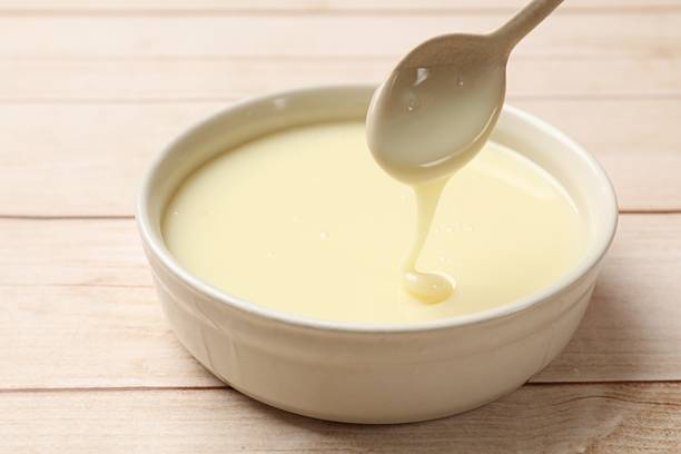istock Condensed milk flowing down from spoon into bowl on wooden table, closeup 2242662864
