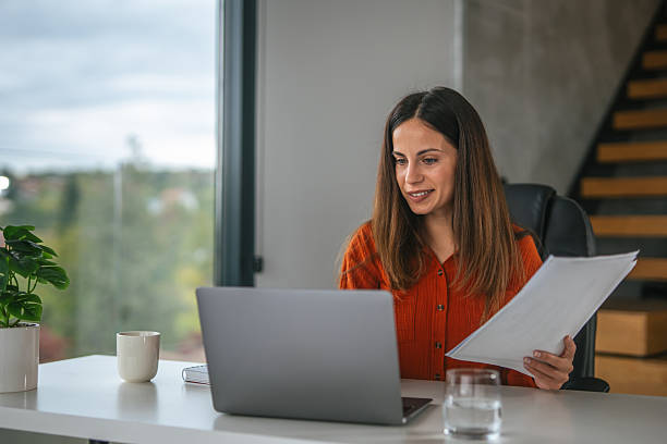 istock Businesswoman reading documents using laptop in home office 2242663888