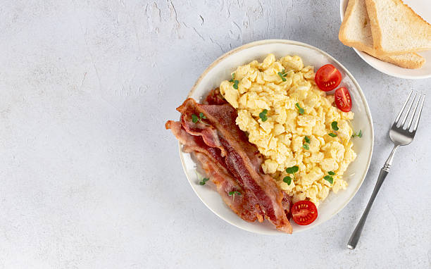 istock Scrambled eggs with crispy bacon and tomatoes on a white background. Top view. Copy space. 2242666130