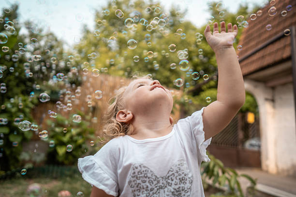 istock Joyful Child Reaches Up Toward Floating Bubbles in a Sunny Backyard Setting 2242668258