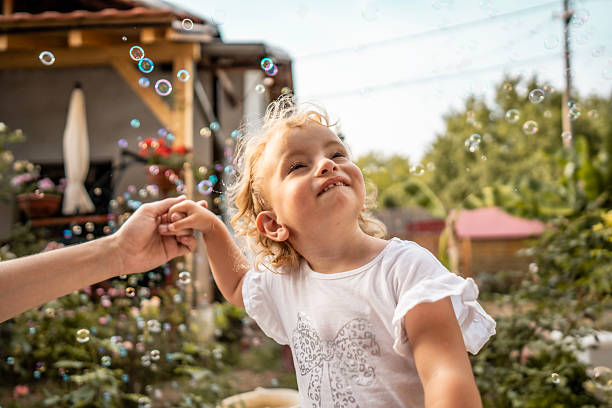 istock Joyful Child Smiling While Chasing Bubbles Outdoors in a Sunny Garden With A Parent Holding Hands 2242669110