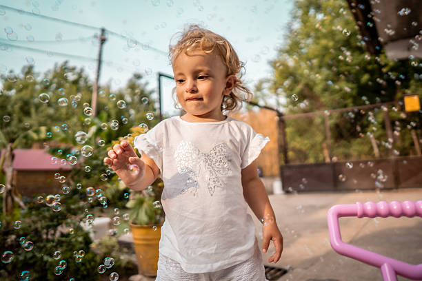 istock Young Child Plays With Bubbles Outdoors On Sunny Day, Delicate Floaties Around White Shirt Butterfly Print 2242669282