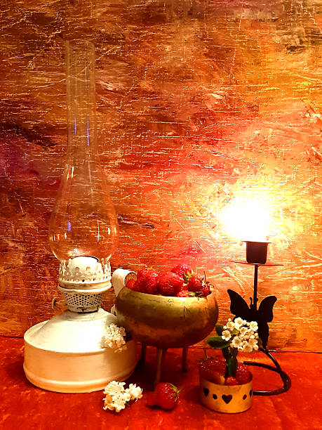 istock Strawberries in a brass container, kerosene lamp, white flowers. Evening romantic still life on a red background, candle in a candlestick. Romance, flowers, elegance, flair. Antique brass 2242672938