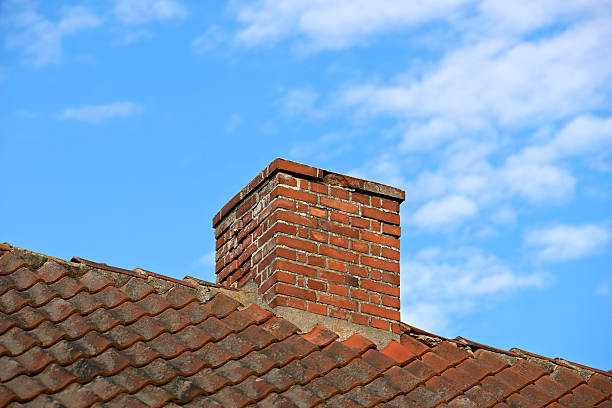 istock Brick Chimney on a Tiled Roof Against a Clear Blue Sky Featuring White Clouds 2242679024