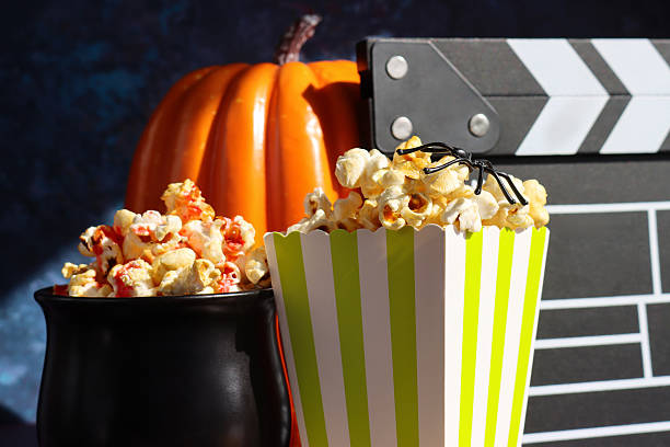 istock Close-up image of plastic spider balancing on popcorn kernels in green and white striped popcorn carton, cauldron film snack food tub, film slate, orange pumpkin background, focus on foreground, Halloween scary film concept 2242691827