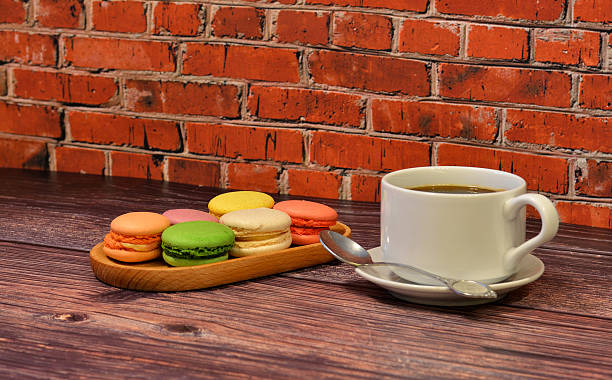 Wooden plate with six colorful macaroons and a cup of hot black tea on a wooden table.