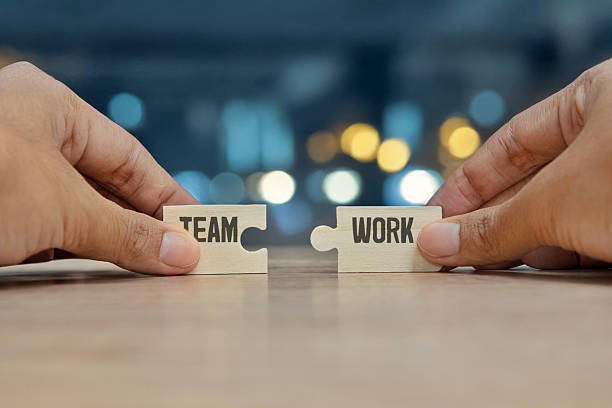 istock Two hands holding wooden puzzle pieces with the words TEAM and WORK. 2242695370