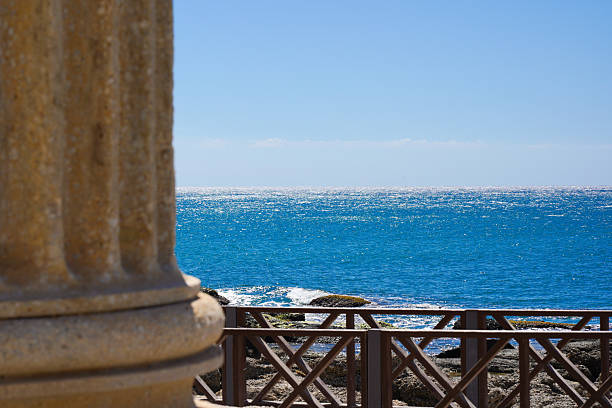 A Serene Coastal View Featuring Crystal-Clear Blue Waters, Rocky Shoreline, and Elegant Architectural Details in the Foreground. Side Antik.