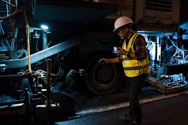 istock Night asphalt recycling roadwork with engineer supervising heavy machinery 2242706046