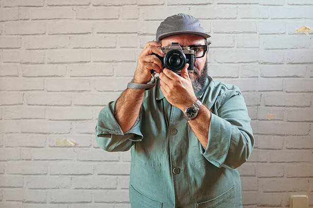 istock Man holding camera taking photo against brick wall. 2242710753