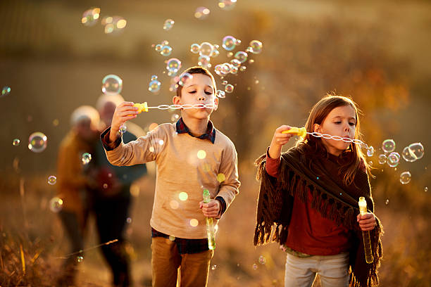 Small siblings having fun with bubble wand during autumn day on a hill. Copy space.