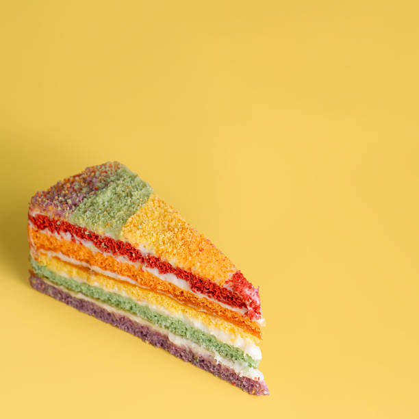 Piece of rainbow cake on yellow background, copy space, 1:1.