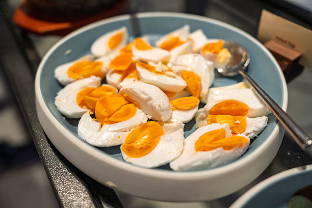 Close-up of salted eggs sliced in half and served in a bowl on a buffet counter. The traditional Asian delicacy features firm whites and rich orange yolks, commonly enjoyed as a side dish or accompaniment in various regional cuisines.
