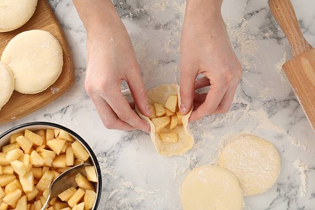 istock Woman making pirozhki (stuffed pastry pies) with apples at white marble table, top view 2242724879