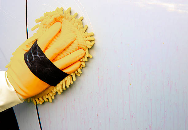 A person is washing the car body with a sponge, using a cleaning agent that causes the rust particles embedded in the car’s paint — which lead to corrosion — to turn purple and be washed away.