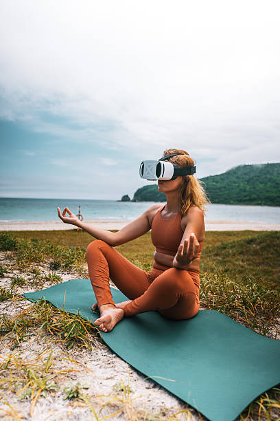 istock Active woman practicing morning yoga on seashore with virtual reality glasses, connecting with nature, charging herself with positive energy. Concept of healthy lifestyle, freedom, modern technology 2242728059