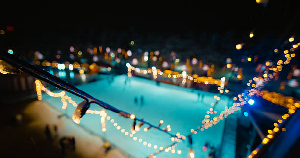 Dark silhouette of female legs in figure skating skates sliding on ice arena. Young woman trains on dark ice rink with blue light. Shiny smooth surface of ice is cut with stripes and scratches from skates. Close up.