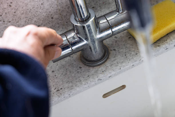 istock Person's hand turning on chrome kitchen faucet with water flowing into white sink 2242746010