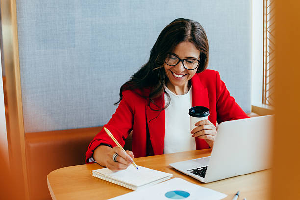 istock Smiling businesswoman working with laptop while taking notes and having coffee 2242747001