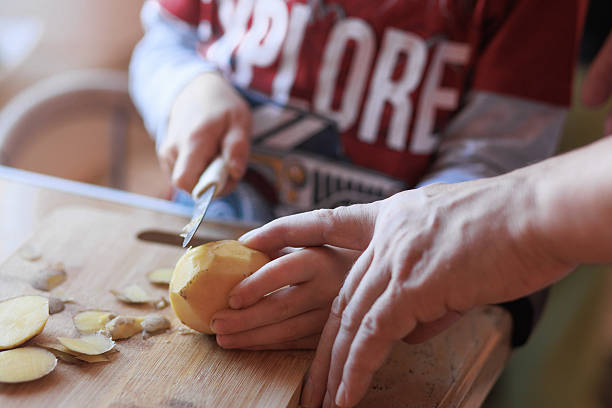 istock Father guiding child while cutting potato at home 2242747436