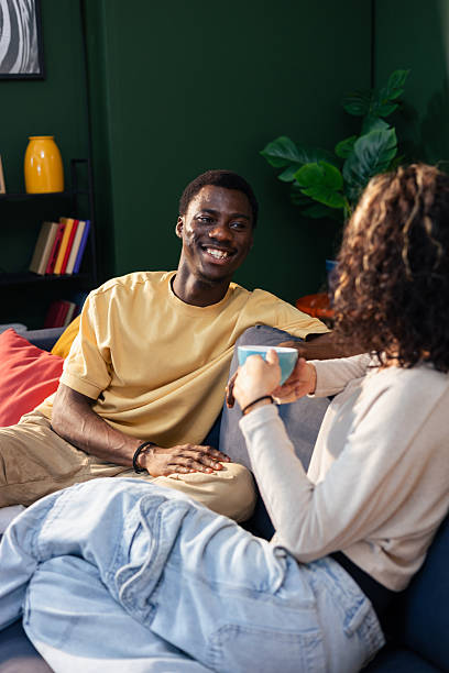 istock Diverse couple smiling, talking, enjoying coffee on sofa 2242749086