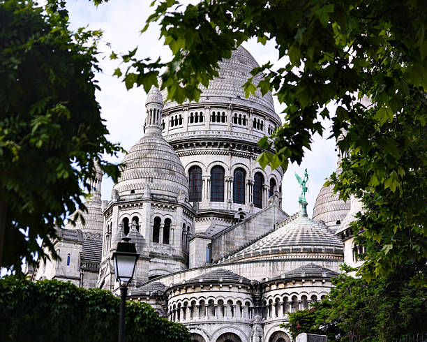 Close view of Sacre Coeur Basilica domes in Montmartre Paris France framed by tree leaves on summer day
