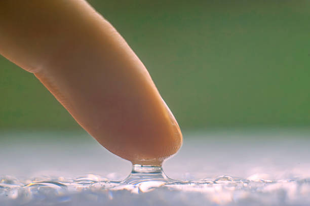 macro photo of a finger touching a drop of water on a table