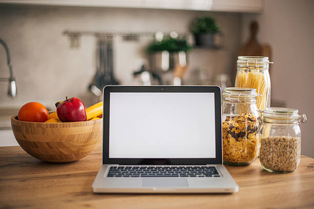 Laptop displaying a blank white screen on a kitchen counter next to healthy fruits and pantry staples
