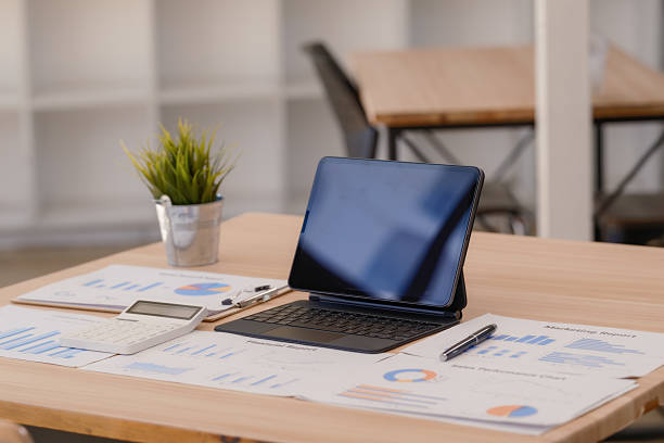 istock A digital tablet with a blank screen and papers with charts and a calculator on a wooden table. 2242759830