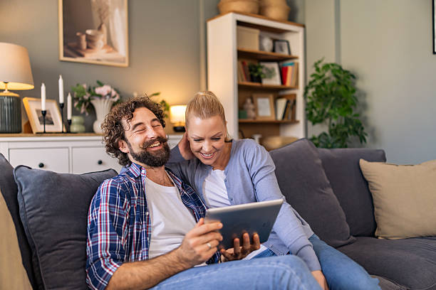 istock A couple watching funny video on the digital tablet and laughing while sitting on the sofa in the living room. 2242769476