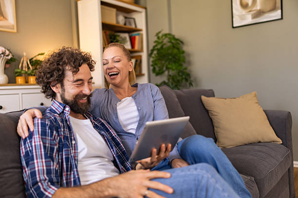 istock A couple watching funny video on the digital tablet and laughing while sitting on the sofa in the living room. 2242769587