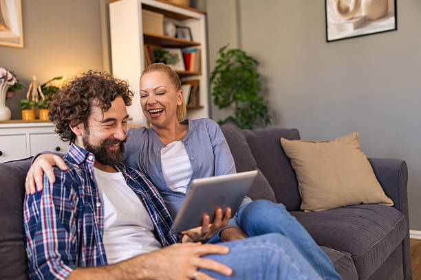 istock A couple watching funny video on the digital tablet and laughing while sitting on the sofa in the living room. 2242769604