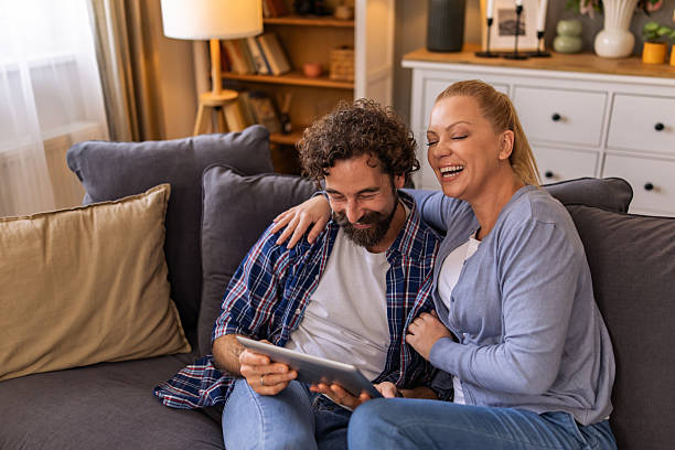 istock A couple watching funny video on the digital tablet and laughing while sitting on the sofa in the living room. 2242769915