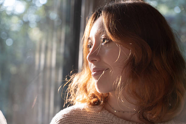 Woman looking out a window, enjoying the warm sunlight on her face